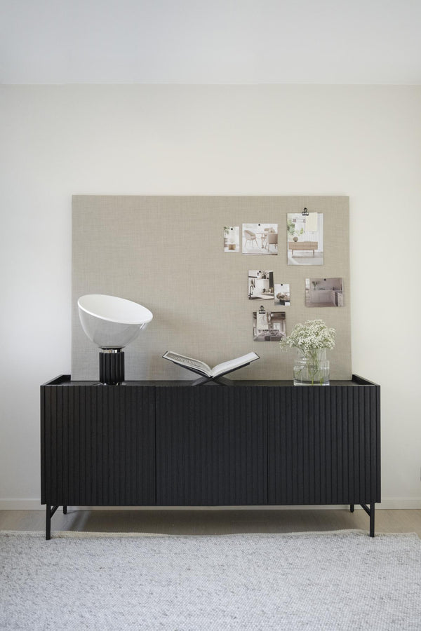 Svart skänk med räfflad front och moodboard med inspirationsbilder, lampa och vas med blommor