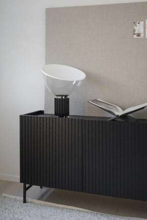Modern bordslampa med vit glaskupa och svart räfflad fot på svart sideboard