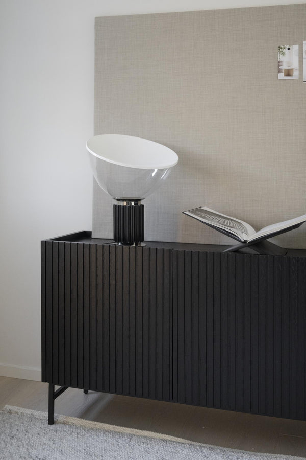 Modern bordslampa med vit glaskupa och svart räfflad fot på svart sideboard