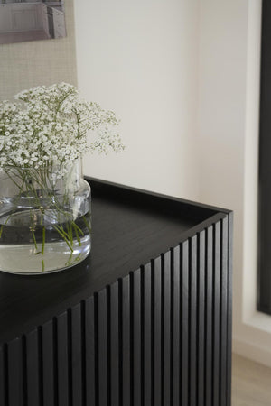 Svart skänk med räfflad front och glasvas med brudslöja, minimalistisk skandinavisk inredning