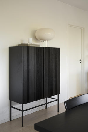 Svart skänk med räfflad front och metallben i moderntrum med krämvit lampa på toppen