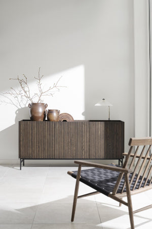 Mörkt träskåp med räfflad front och svarta ben, dekorerat med keramikkrukor och torkade grenar i minimalistisk inredning