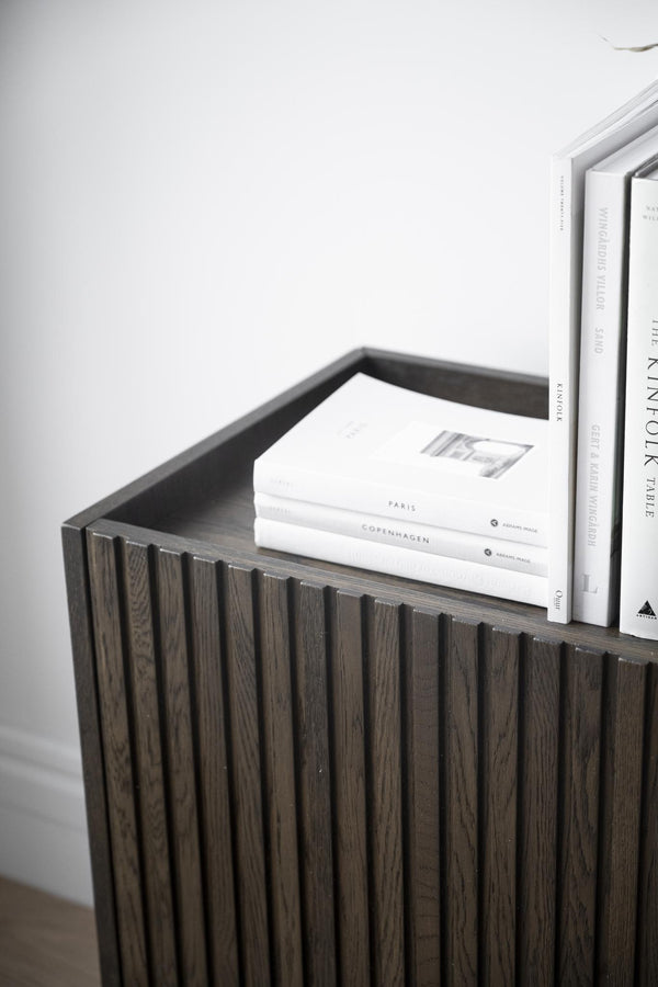 Mörkbrun trähylla med räfflad front, dekorerad med vita designböcker om Paris och Köpenhamn