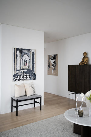 Minimalistiskt vardagsrum med sittbänk, konst och Buddha-staty på svart skänk
