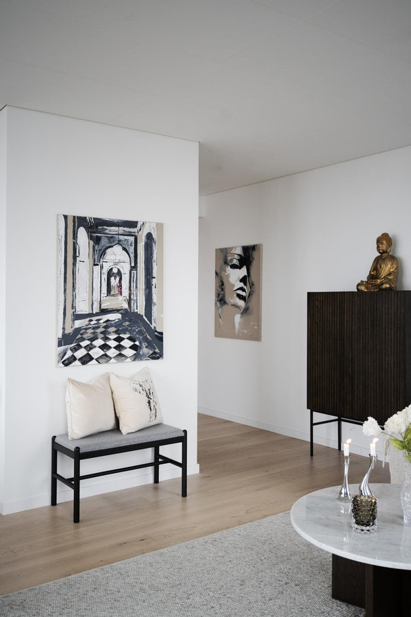 Minimalistiskt vardagsrum med sittbänk, konst och Buddha-staty på svart skänk