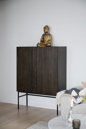 Mörkt skåp med räfflad yta och svart metallställning, dekorerat med gyllene Buddhastatyn i vardagsrum