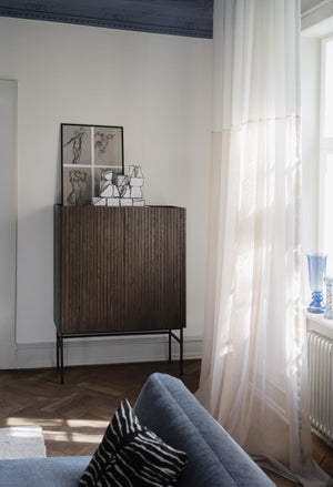 Skåp i mörkt trä med räfflade dörrar på svart stativ, dekorerat med konstverk och glasvaser i ljust vardagsrum