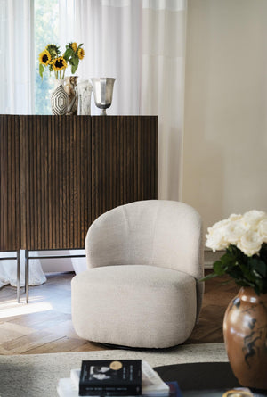 Beige fåtölj i teddy-tyg framför mörkt träskåp med dekorativa vaser och blommor i elegant vardagsrum