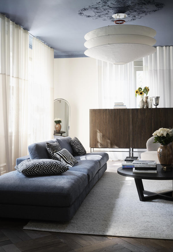 Modernt vardagsrum med grå soffa, rund lampskärm, flutade gardiner och sideboard i trä
