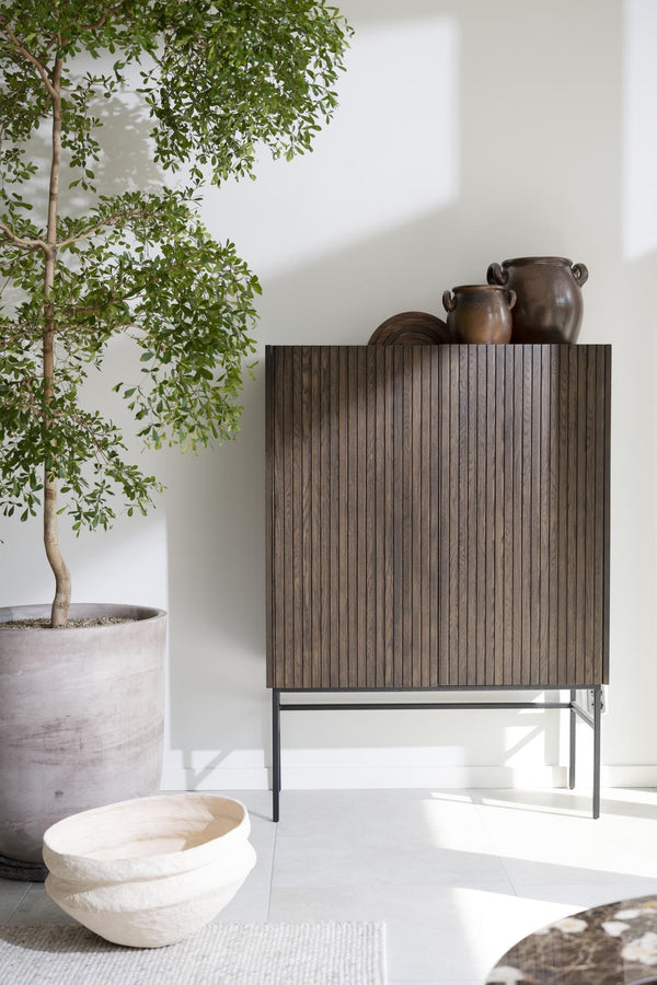 Sideboard med räfflad träfront på metallben, dekorerat med keramikkrukor, bredvid grön växt i kruka