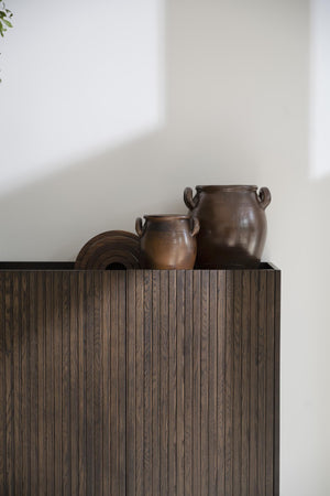 Dekorativa bruna krukor i keramik på skåp med vertikala ribbor i mörkt trä