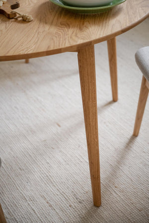 Runt matbord i oljad ek med tre slanka ben på ljus matta, skandinavisk design