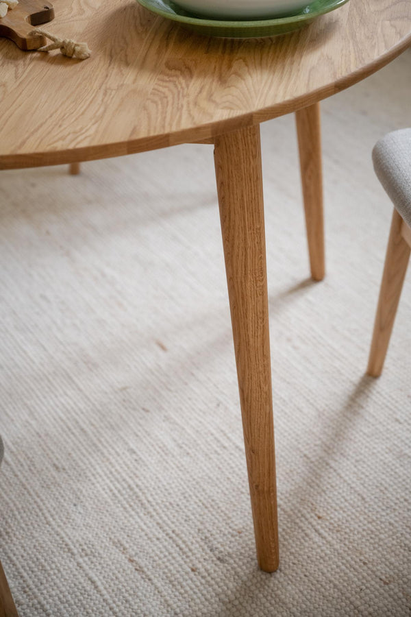 Runt matbord i oljad ek med tre slanka ben på ljus matta, skandinavisk design