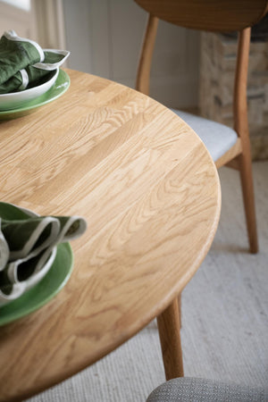 Runt matbord i ljust trä med synlig ådringsmönster, uppdukat med gröna tallrikar och servetter