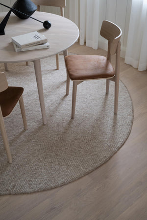 Rund ljus bordsmatta i jute under matbord med stol i trä och rosa dyna i skandinavisk inredningsstil