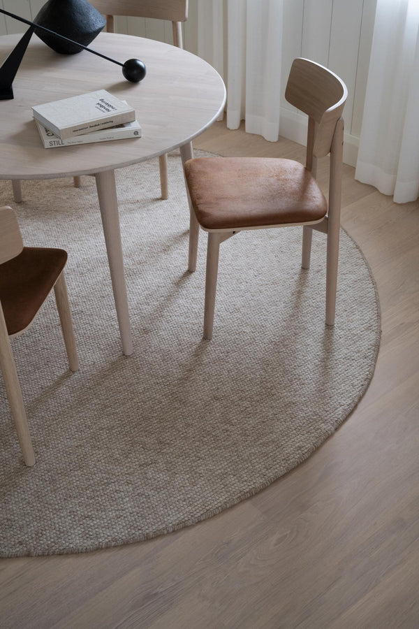 Rund ljus bordsmatta i jute under matbord med stol i trä och rosa dyna i skandinavisk inredningsstil