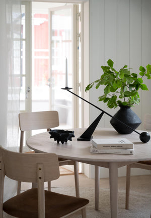 Ljust matbord i trä med ljusstake, böcker och vas med gröna kvistar i modern skandinavisk inredning