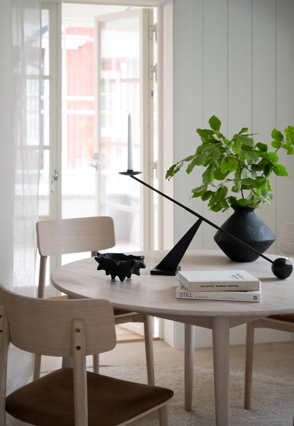 Ljust matbord i trä med ljusstake, böcker och vas med gröna kvistar i modern skandinavisk inredning