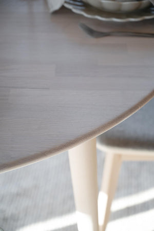 Närbild på ljust träbord med synlig kant och bordsben i naturligt trä, porslin i bakgrunden