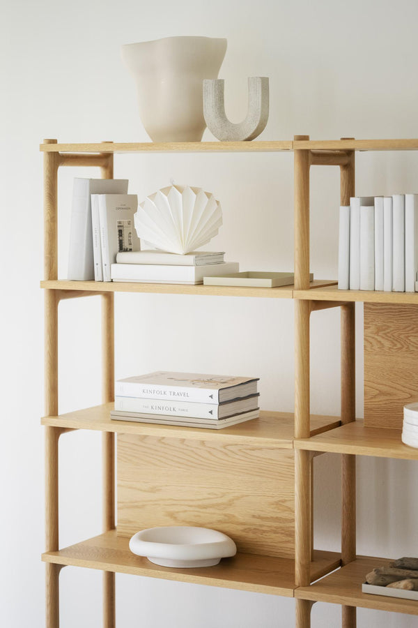 Trädhylla i ljust trä med böcker och vita dekorationsobjekt i skandinavisk stil