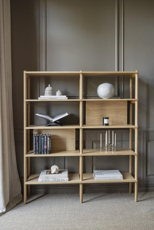 Bokhylla i ljust trä med åtta fack, stylad med böcker och dekorativa föremål mot grå vägg