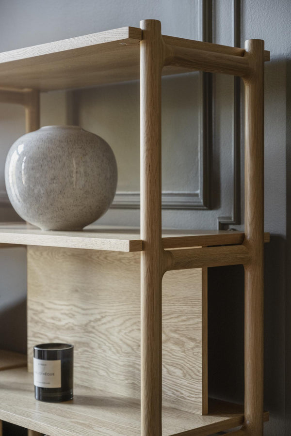 Minimalistisk hylla i ljust trä med runda ben, dekorerad med keramikvas och doftljus i skandinavisk stil