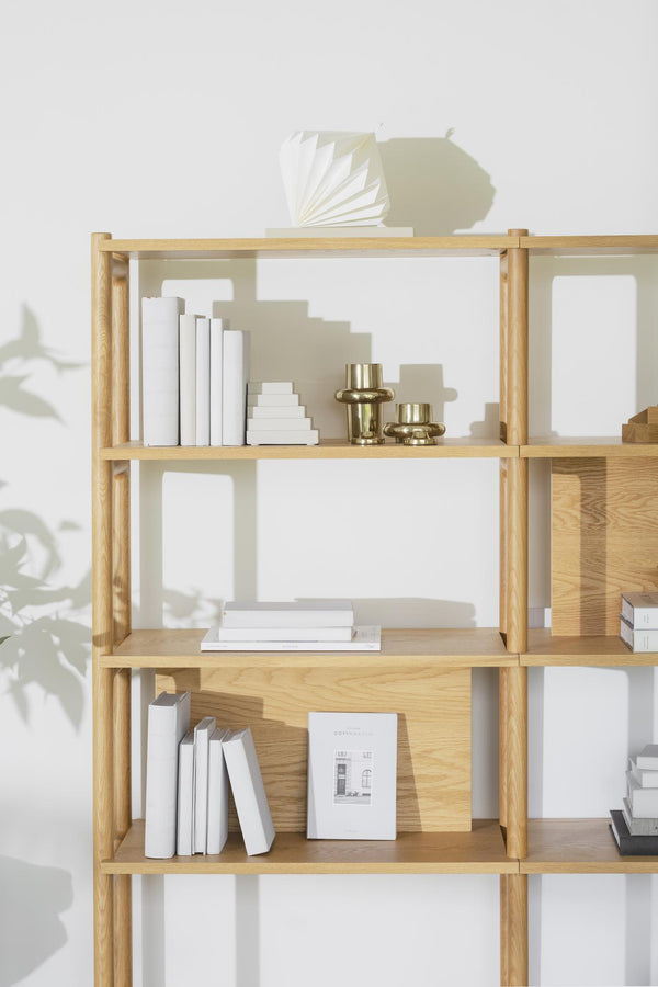 Ljus bokhylla i trä med vita böcker och dekorativa föremål i minimalistisk skandinavisk stil