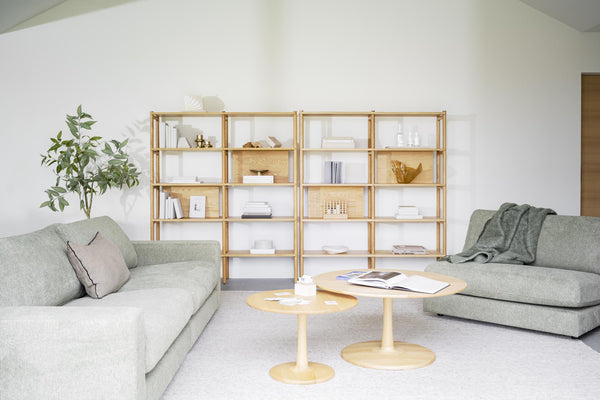 Ljust vardagsrum med gröna soffor, träbokhylla och runda soffbord i skandinavisk design