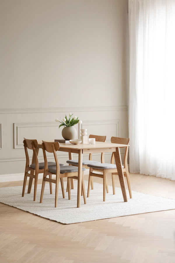 Ljus matgrupp i trä med fyra stolar och grå dynor på vit matta i minimalistisk matsal