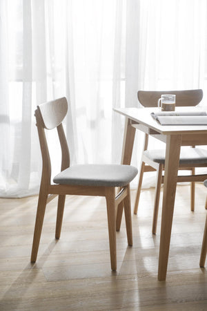 Moderna matstolar i ljus ek med grå sits vid matbord i skandinavisk stil