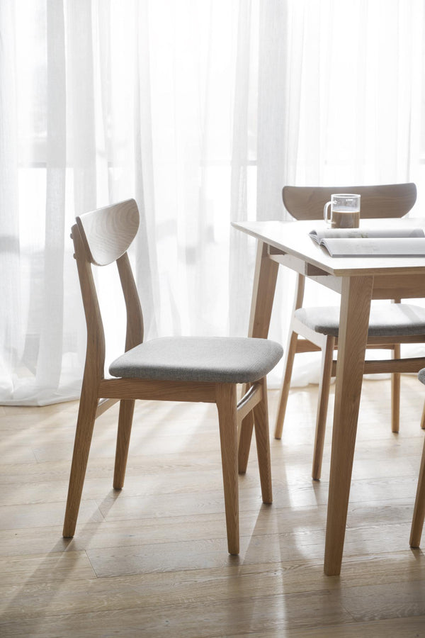 Moderna matstolar i ljus ek med grå sits vid matbord i skandinavisk stil