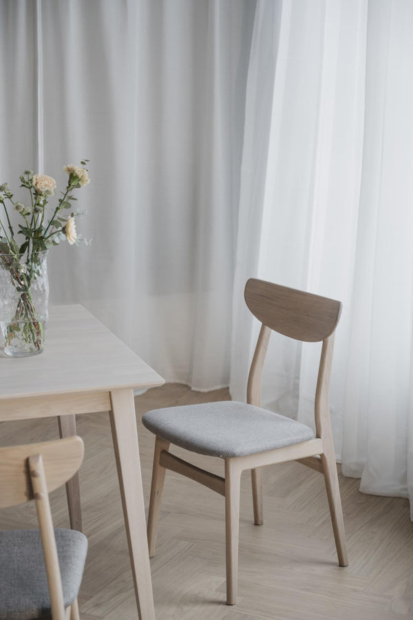 Ljus trämatstol med grå stoppad sits vid matbord i skandinavisk minimalistisk inredning