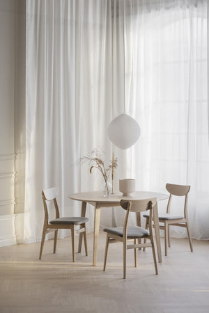 Rund matbord i ljust trä med fyra stolar och vit taklampa i minimalistisk skandinavisk matsal