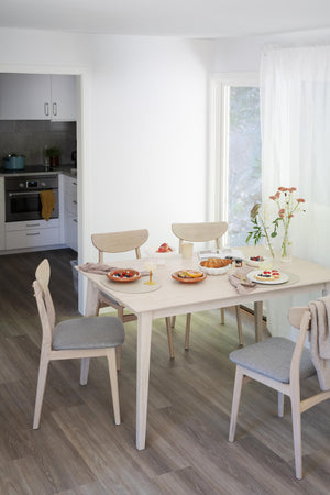 Matgrupp med vita stolar och grå dynor vid dukad frukostbord i ljust kök med fönster