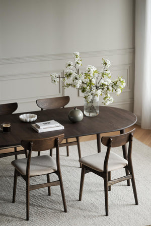 Runt matbord i mörk ek med matchande stolar och beige klädsel i skandinavisk matsal