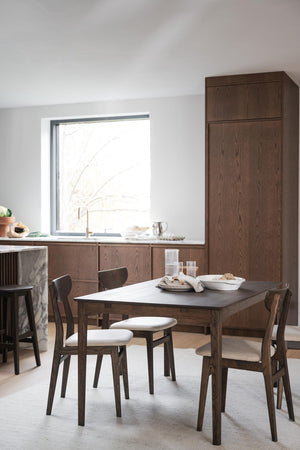 Matbord i mörkt trä med stolar och vita dynor i modern minimalistisk matsal med höga skåp