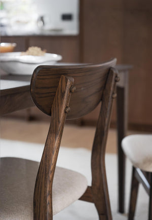 Närbild på ryggstöd av mörkbrun trässtol vid matbord med tallrikar i suddig bakgrund