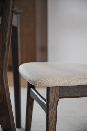 Närbild på stolsits i beige tyg med mörkt träben och ryggstöd i skandinavisk design