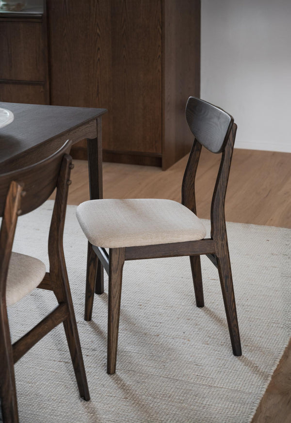 Matsalsstol i mörkbejtsad ek med beige stoppad sits och rygg, placerad vid matbord i modern skandinavisk stil