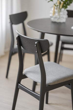 Svarta trämatstolar med grå stoppade sitsar vid runt matbord i modern skandinavisk stil