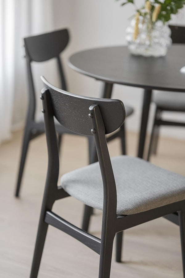 Svarta trämatstolar med grå stoppade sitsar vid runt matbord i modern skandinavisk stil