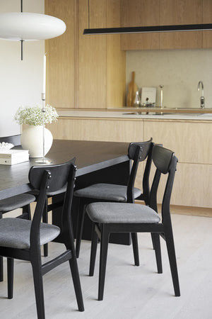 Svart rund matbord med grå stoppade stolar i modern skandinavisk matsal med ljust trä kök