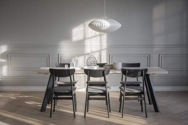 Modern matgrupp med svarta stolar och vit taklampa i ljust matrum med puts och parkettgolv