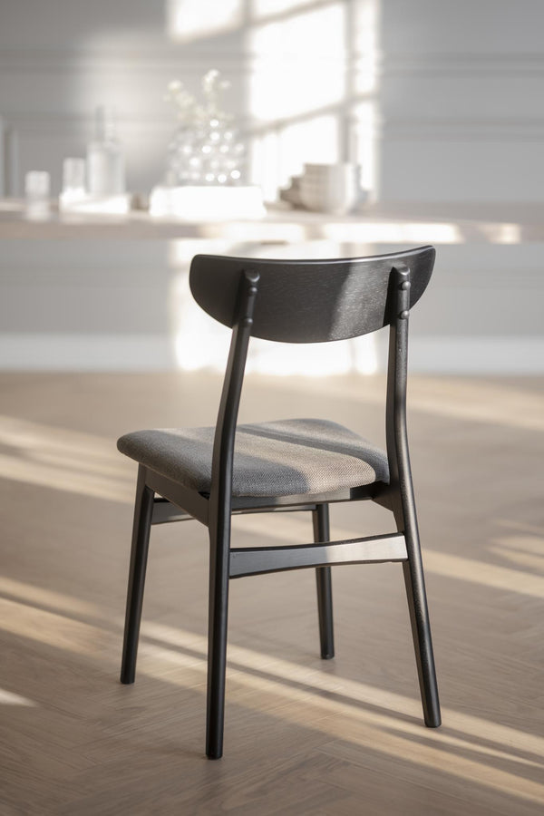 Svart trätstol med grå stoppad sits i modern matsal med ljusinsläpp från fönster