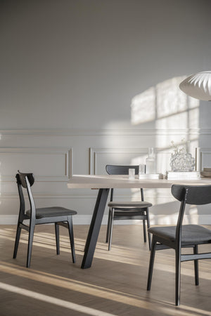 Matbord i ljust trä med svarta stolar i modern skandinavisk matsal med naturligt ljusinsläpp