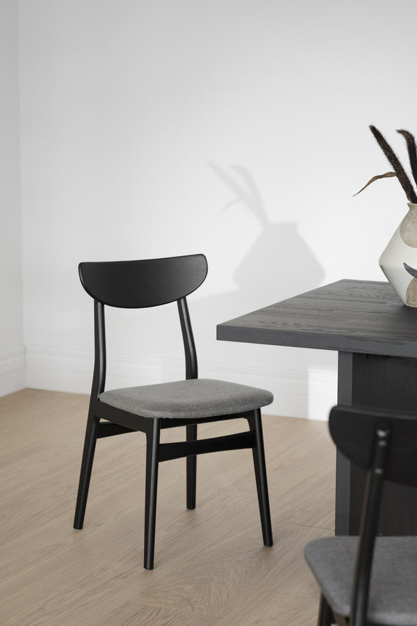 Svart matstol med grå stoppad sits och träryggstöd vid matbord i modern skandinavisk stil