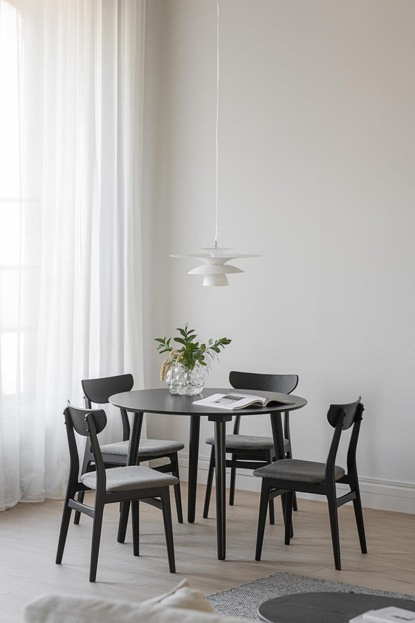 Matgrupp med runt svart bord och fyra stolar i minimalistisk skandinavisk matsal med vit pendellampa