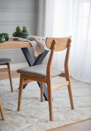 Matstol i ek med grå stoppad sits vid matbord i ljus matsal med textilmatta