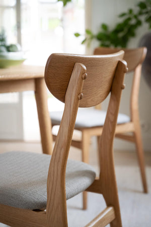Närbild på matstol i ljus ek med svängd rygg och grå sits vid matbord i skandinavisk stil
