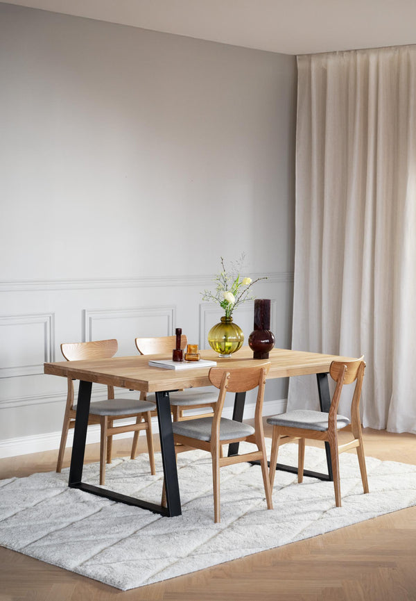 Matbord i ljust trä med svarta ben och fyra stolar med grå dynor i modern matsal